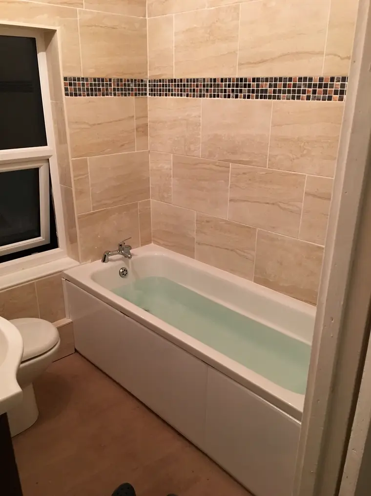 Bath and toilet in a bathroom tiled in cream with a mosaic border